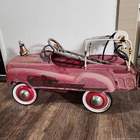 Side view showing pink body with Riley's Fire Dept decal, bell on hood, rust on ladder and frame, whitewall wheels with red rims.