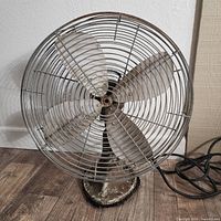 Front view of vintage metal oscillating fan showing metal protective grille and four metal blades with wear and patina.