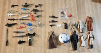 Full collection of vintage Star Wars and GI Joe toy weapons and figures arranged on wooden floor