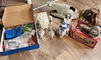 Overview of several vintage Kenner Star Wars vehicles and playsets: AT-ST, Slave I, R2-D2 figure, boxed items including Death Star playsets, and more on wooden floor.