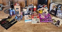Wide overview photo showing the entire lot including boxes, figures, posters, promotional cups and reading materials on a wooden floor.