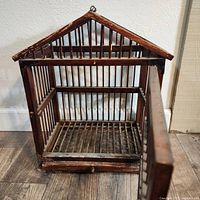 Front angled view showing the interior and peaked roof design of the vintage wooden birdcage with door open.