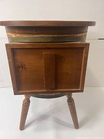 Front view of wooden barrel side table showing the door closed and legs.