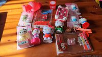 15 Hello Kitty and Sanrio character toys and knick-knacks displayed on wooden surface, some in packaging, some loose.