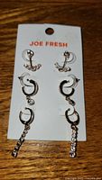 Full view of the 3 pack Joe Fresh earrings on branded card on wooden surface.