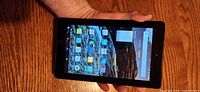 Front view of the Amazon Fire Tablet 7 showing the screen turned on with app icons visible. Device held in one hand showing size and screen condition.