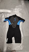 Full view of the Body Glove shorty wetsuit, showing black body with blue side panels and short sleeves and legs, laid flat on bubble wrap.