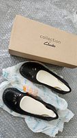 Pair of black perforated leather ballet flats with decorative cutouts on toe, shown with their box labeled Clarks Collection.