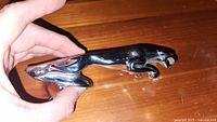 Jaguar hood ornament held in hand showing side profile with visible surface condition and metallic finish.