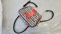Overall view of small rectangular purse with Juicy Couture text and red heart pattern, black strap laid out flat.