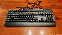 Full front view of Lenovo black wired keyboard on wooden surface showing the entire keyboard layout including numeric keypad and cable with USB connector.