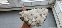 Front side of the white crystal geode showing dense cubic crystals on dark rock base, held in hand for scale.