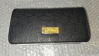 Front view of Michael Kors black women's wallet with embossed logo pattern and gold-tone plaque