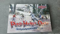 Front of the Monopoly Pond Hockey-Opoly 2nd edition board game box showing pond hockey players in snowy outdoor setting.