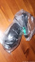 Black PS2 laser mouse sealed in clear plastic bag on wooden surface, showing green PS2 connector cable.