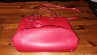 Side bottom view of red leather handbag showing condition and metal feet on base.