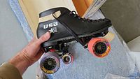 Close-up of one black Riedell USA roller derby skate held in hand, showing Mad Hog 62mm speed wheels in multicolor.