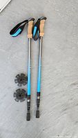 Pair of hiking poles showing cork handles, blue and black shaft, and basket attachments underneath.