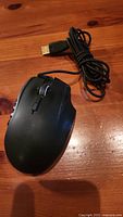 Black wired Razer Naga laser gaming mouse with braided USB cable on wooden surface.