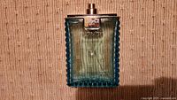 Front view of blue glass perfume bottle with about 3/4 full light greenish-blue liquid, silver accent top plate with Versace branding