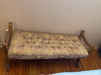 Upholstered wooden bench showing front and part of the armrests, fabric with floral pattern, some staining visible on seat cushion.