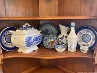 Full view of all items on wooden shelf showing the soup tureen, plates, bowl, bottle, and jar