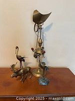 Photo of brass decorative items including oil lamp and animal figurines on table.