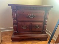 Front view of wood cabinet showing two drawers with decorative metal handles and carved column-style sides.