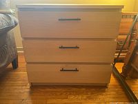 Front view of the wooden cabinet showing three drawers and black handles.
