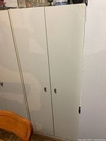 Closed white storage cabinet with two doors and metal handles, placed near wooden furniture.