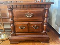 Front view of the wood cabinet showing three drawers with brass handles and decorative turned columns