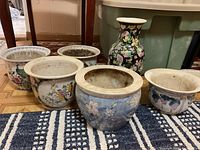 Front view of six ceramic planters and a vase showing decorative floral and bird motifs and signs of wear
