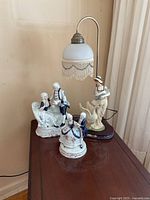 Photo of ceramic figurines and table lamp turned off on a wooden side table.