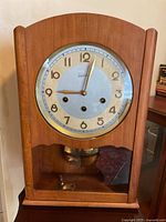 View of the full wooden wall clock showing the clock face, pendulum, and key inside the case.
