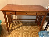 Front view of wooden desk showing three drawers with round knobs and support bars between legs.