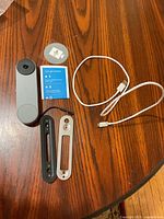 Photo of Google Nest doorbell, mounting brackets, USB cable, manual, and sticker on wooden surface.