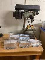 Full view of Delta drill press on bench with drill bits in Ziploc bags laid in front.