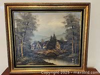 Full view of framed landscape painting showing stone bridge, houses and trees in outdoor scene.