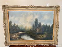 Full view of the framed oil painting showing a forest and river landscape with ornate gold frame.