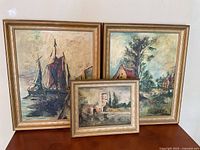 Three framed oil paintings displayed together showing maritime and landscape scenes.