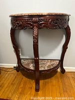 Front view of semicircular hall table showing marble top and carved floral wooden apron with three legs and lower marble shelf.
