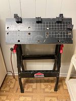 Front view of Jobmate workbench showing measuring grids, holes, clamps, and red handles on legs.