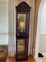Full view of tall wooden lighted display cabinet with glass inserts and carved top.