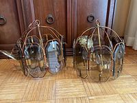 Pair of metal framed pendant light fixtures each with six curved glass panels. Shows use wear and patina on the metal. Wood floor background.