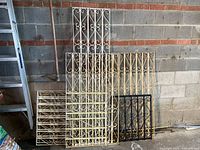 Metal gate and fence panels laid against a wall, showing various white and black decorative metalwork pieces with scroll designs and some rust/weathering.