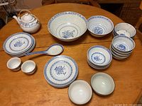 Wide view showing nearly all blue and white china dishware items on table, including teapot, large bowls, plates, spoons, and small cups.
