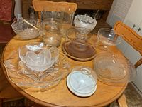 Overview of multiple clear glass serving bowls and plates on a wooden table including some with floral and leaf designs, showing the full set.