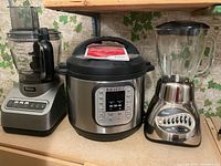 Front view of three kitchen appliances on a counter: Ninja food processor, Instant Pot Duo, Oster blender