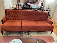 Full view of large vintage orange sofa with tufted back and wooden legs, set in living room.
