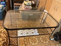 Front angled view showing the glass top and the decorative metal lower shelf with floral and geometric patterns.